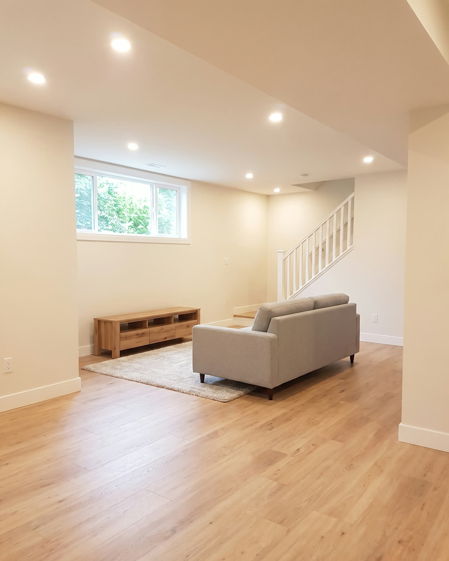 Illustration of a finished, brightly lit basement family room with light wood-look flooring and pot lights