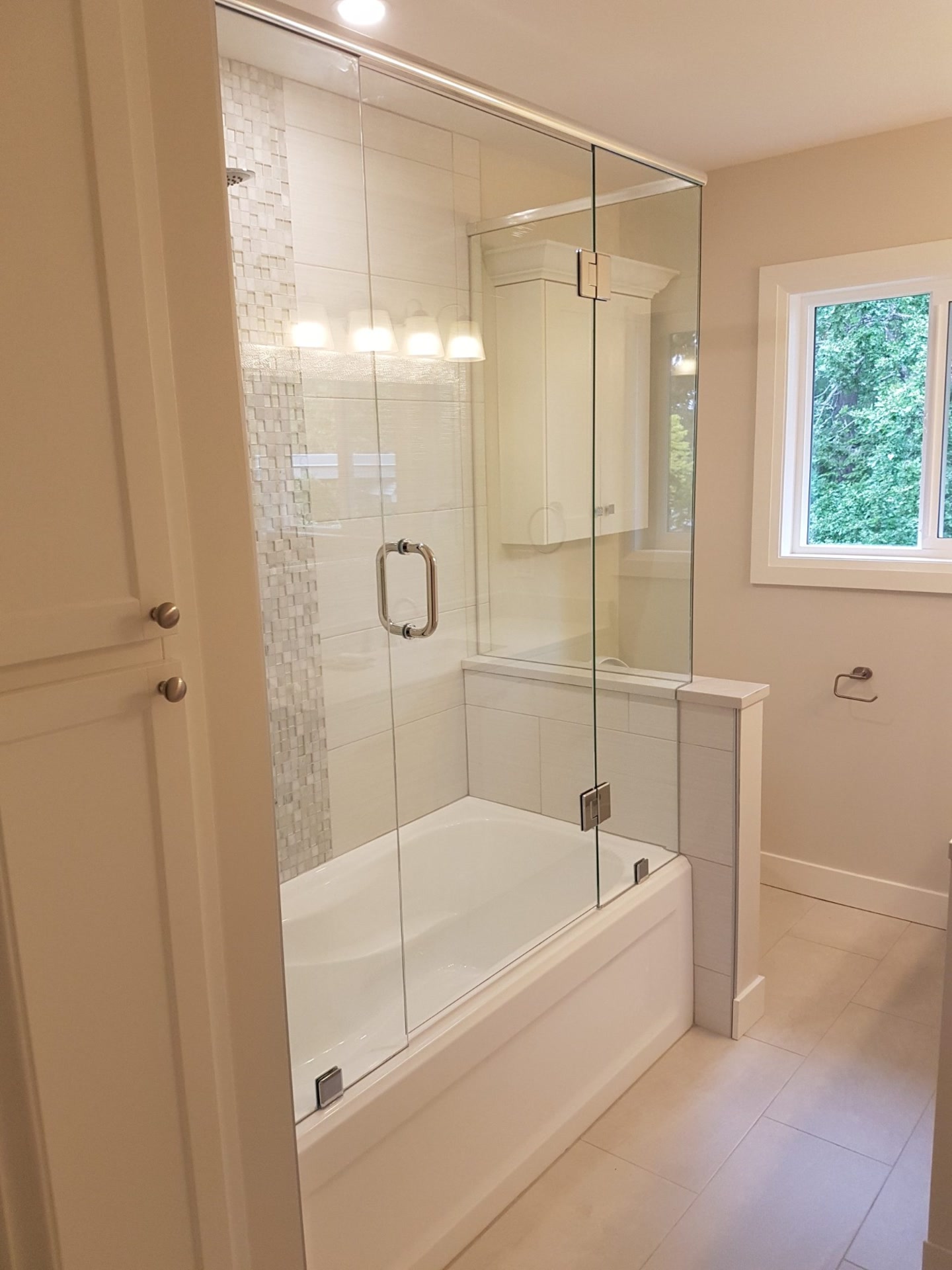 Bathroom with a tub and shower behind a single frameless glass panel, window beyond