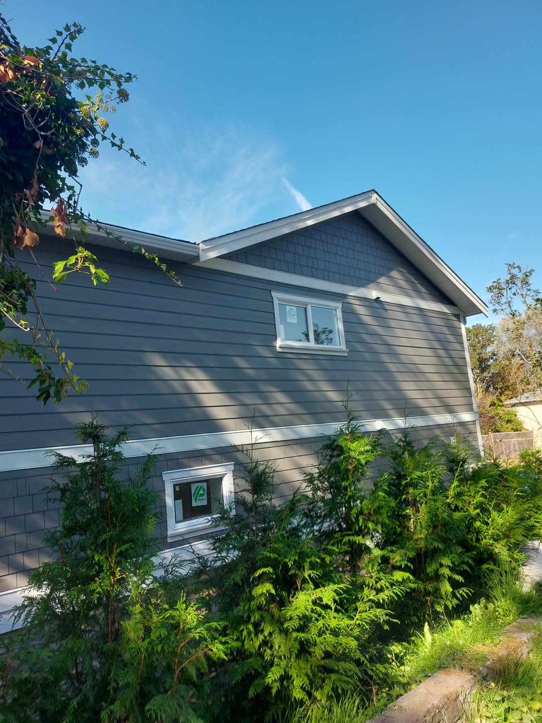 Gable end of the same house, new grey shingle siding and white trim behind the garden